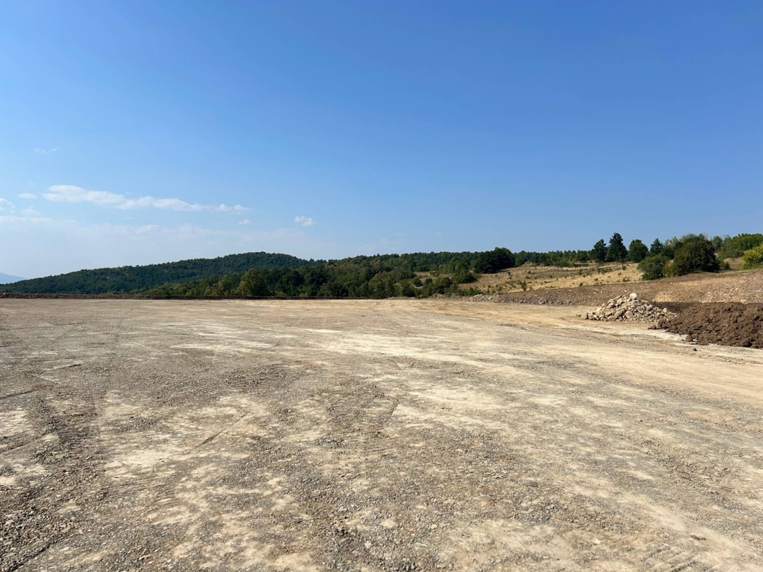 Širok poravnat plato na Malka Golaji, sa gomilom kamenja i nasipom zemlje uz desnu ivicu i šumom na horizontu; nema nijedne mašine.